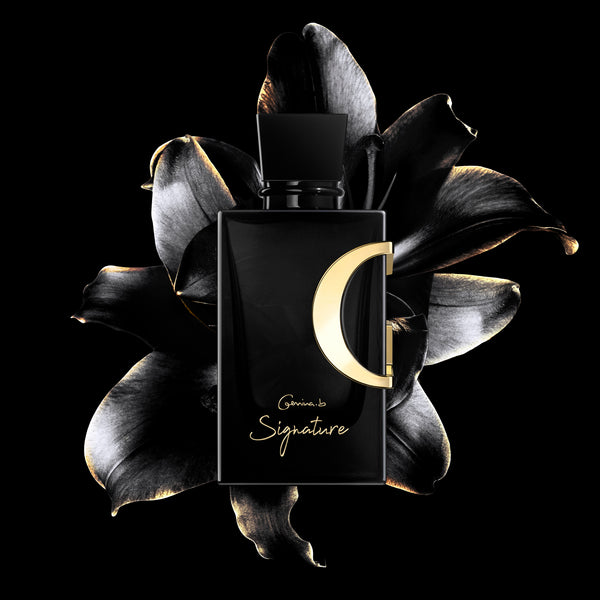 A black perfume bottle with a gold 'G' logo, placed on a surface with black floral elements around it.