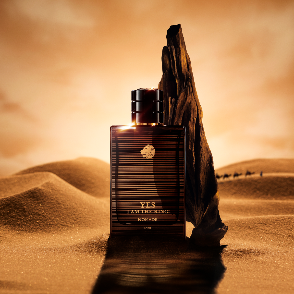 Perfume bottle labeled 'YES I AM THE KING NOMADE' in a desert setting with sand dunes and a sunset.